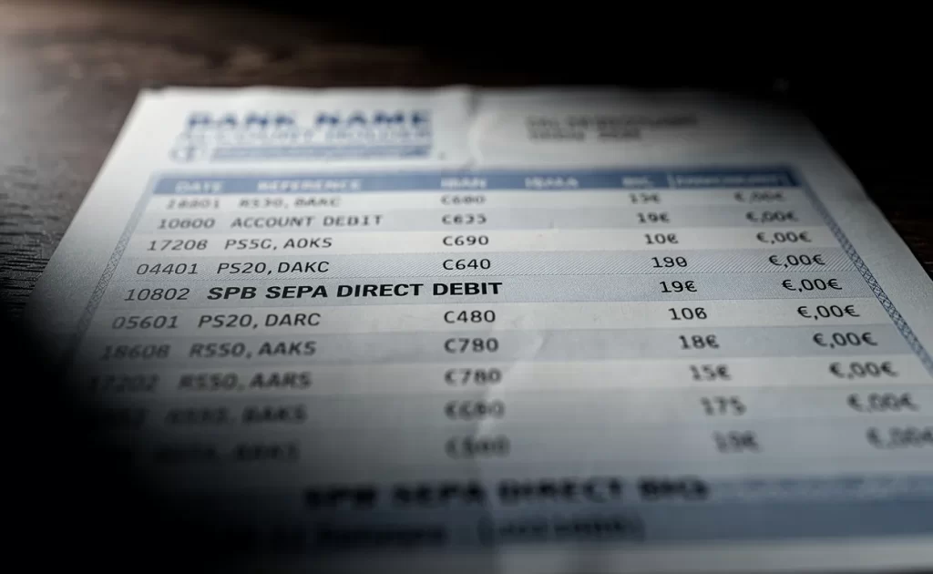 Gros plan photoréaliste d’un relevé bancaire européen montrant une ligne de prélèvement SPB SEPA dans une lumière contrastée.