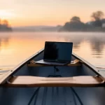 Un canoë élégant flotte sur la rivière Cher au lever du soleil, avec un ordinateur portable ouvert sur le siège en bois et des reflets colorés sur l’eau calme.