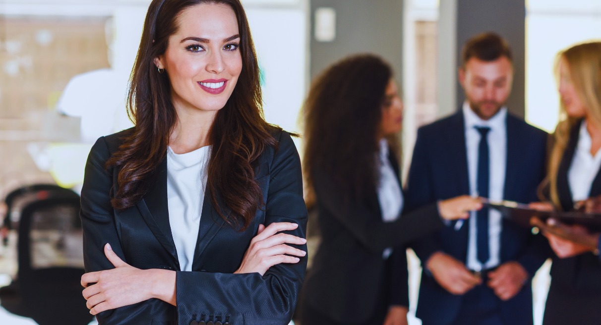 Femme manager souriante bras croises devant son equipe dans un bureau