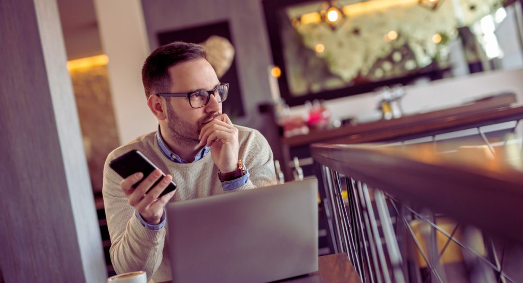 Homme consultant independant avec lunettes tenant un smartphone devant un laptop