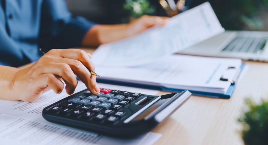 Personne utilisant une calculatrice avec des documents fiscaux et un clipboard sur un bureau
