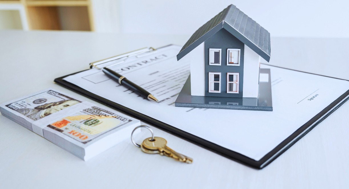 Maquette de maison posée sur un contrat immobilier, à côté de billets et d'un trousseau de clés